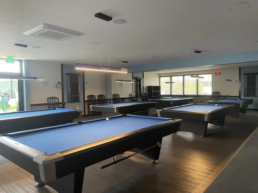 Billiards room in Leisure World Seal Beach featuring multiple blue pool tables and seating areas, promoting social engagement and recreational activities for residents.