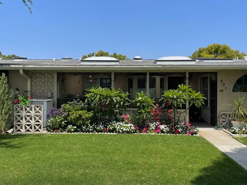 Condominium exterior in Leisure World Seal Beach, featuring landscaped garden, vibrant flowers, and clear blue sky, representing potential homeownership in a 55+ community.