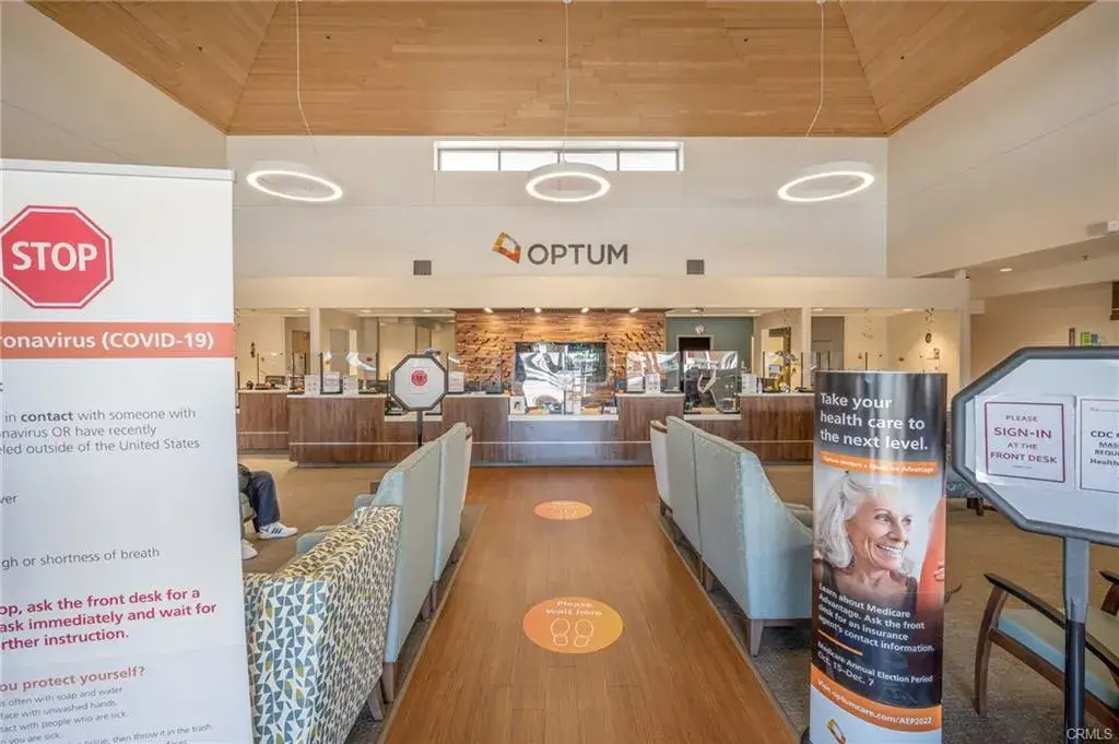 Healthcare center reception area with signage about COVID-19 precautions, welcoming atmosphere, and informational banners promoting health services, emphasizing community wellness and accessibility for Leisure World residents.