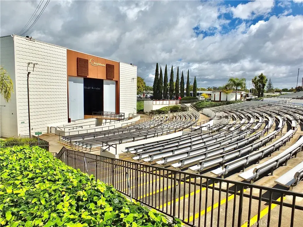 Amphitheater at Leisure World Seal Beach, featuring tiered seating and a stage, surrounded by greenery and palm trees, designed for community events and performances.