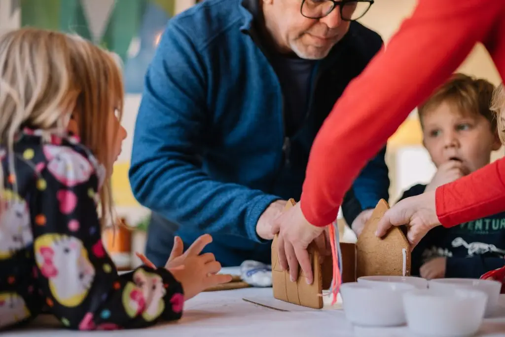 Family members building a gingerbread house together, showcasing a collaborative holiday activity with children engaged in creative fun.