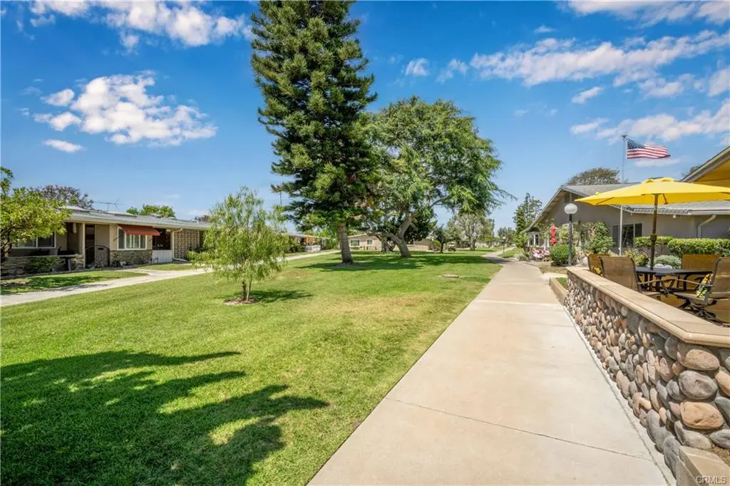 Pathway through Leisure World Seal Beach community, featuring manicured lawns, well-maintained homes, and outdoor seating under an umbrella, showcasing the inviting atmosphere for seniors.