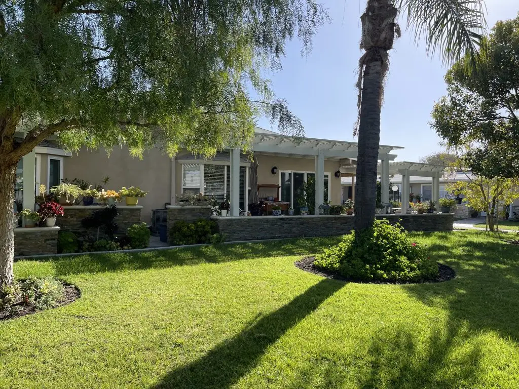 Senior living community home in Leisure World Seal Beach, featuring landscaped gardens, palm trees, and outdoor seating areas, highlighting affordability and amenities for retirees.