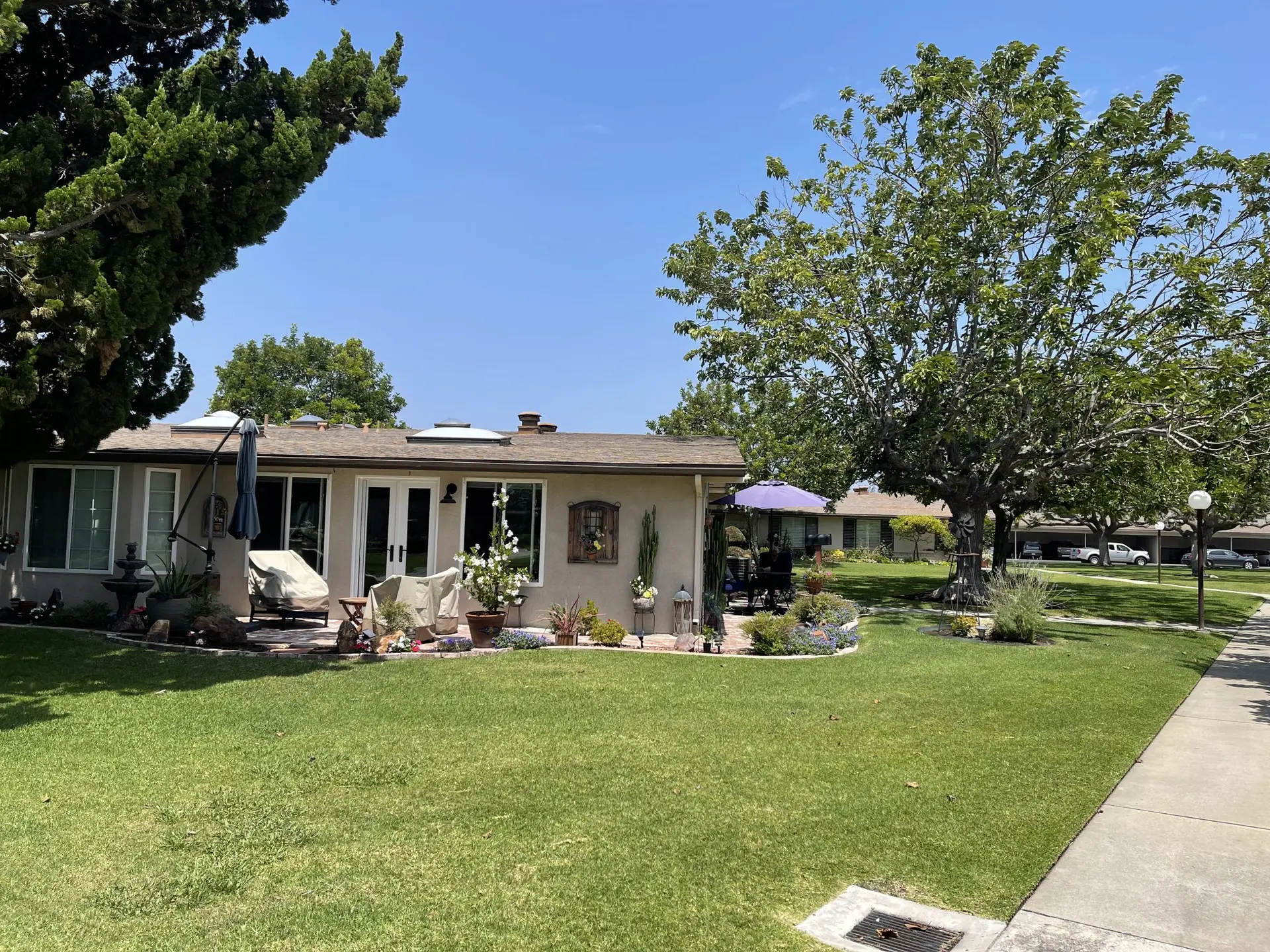 Leisure World Seal Beach home exterior with landscaped yard, seating area, and nearby trees, showcasing community living for seniors.