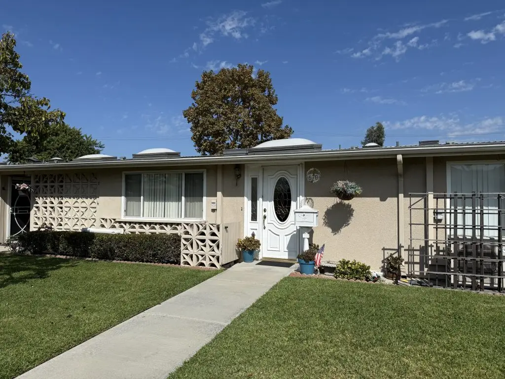 Exterior view of a Leisure World home featuring a landscaped front yard, a white door with decorative glass, and a mailbox, representing the 55+ community real estate market.