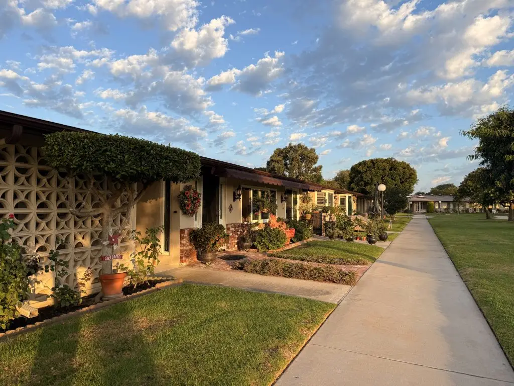 Cooperative housing units in Leisure World Seal Beach with landscaped gardens, walkways, and a clear blue sky, reflecting the community's appeal for active adults.