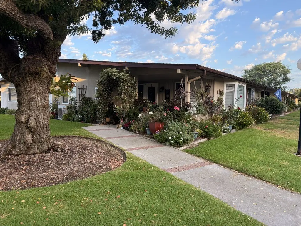 Charming Leisure World home with landscaped garden, pathway, and mature tree, showcasing community living and outdoor space.