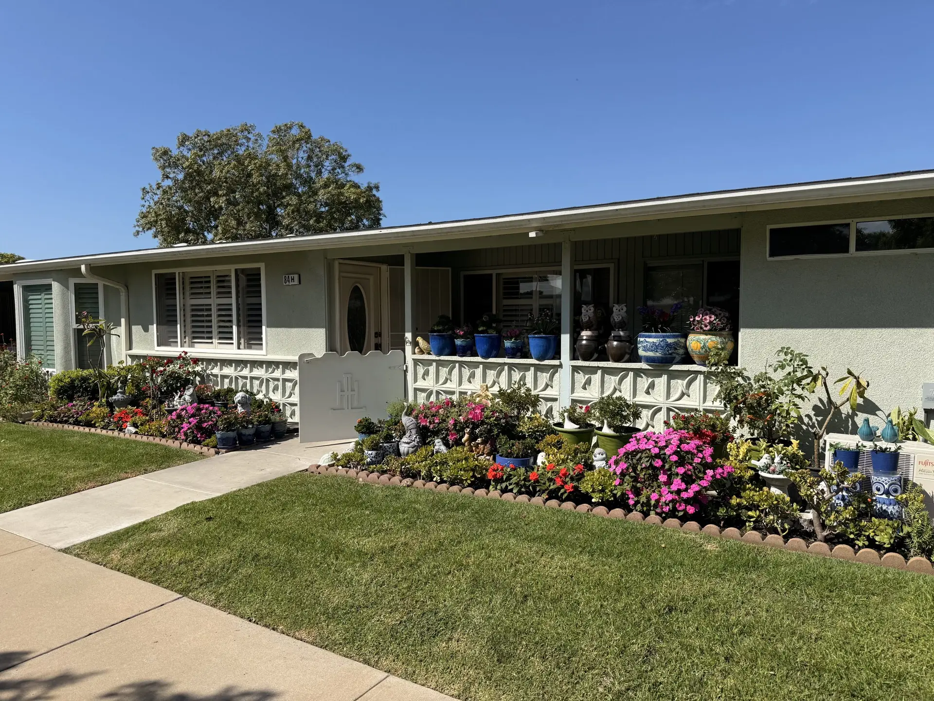 Charming Leisure World Seal Beach home with vibrant flower garden and decorative pots, showcasing community aesthetics and curb appeal.