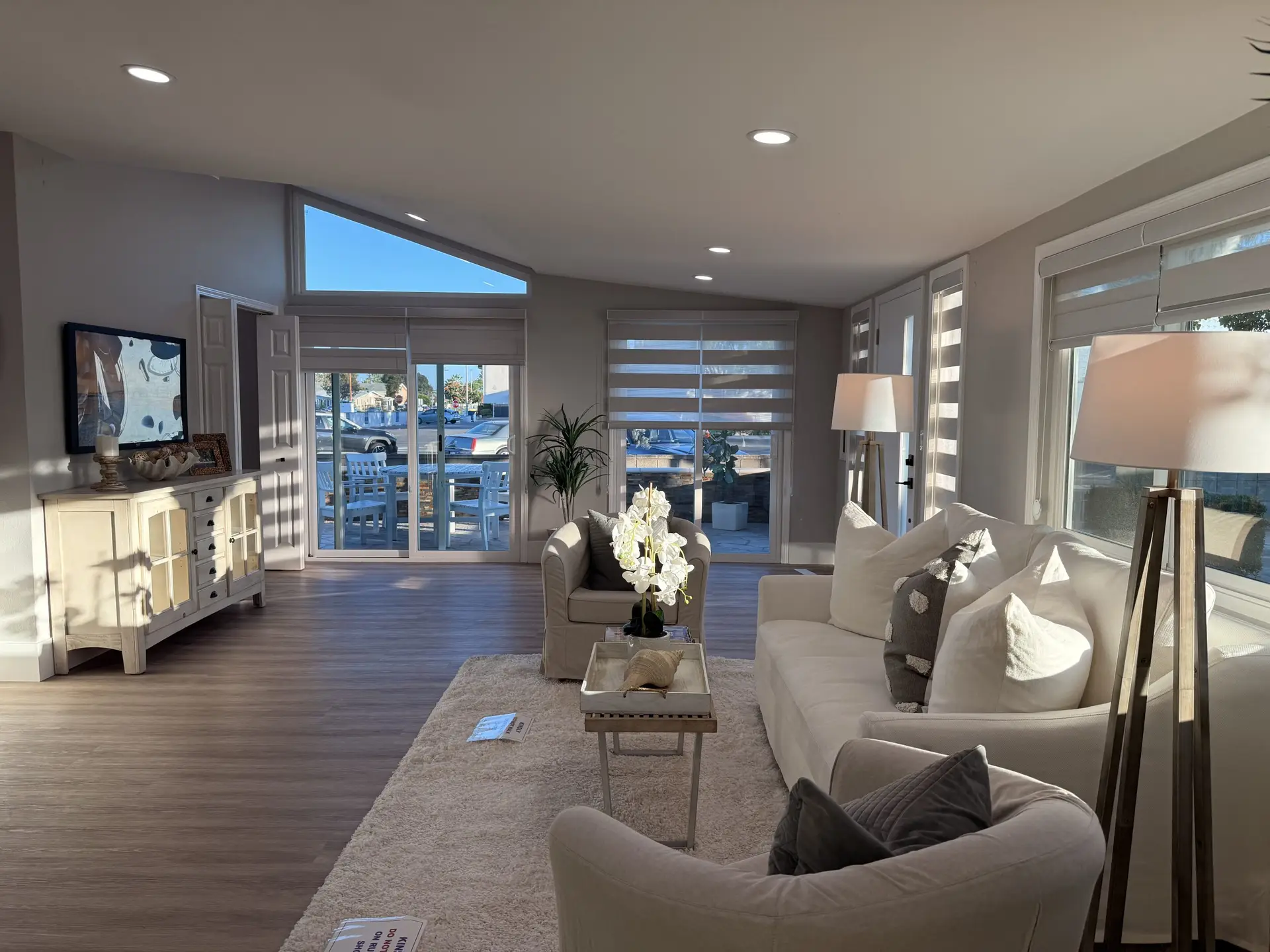 Bright, modern living room in Leisure World Seal Beach featuring white furniture, decorative pillows, and large windows with outdoor views, highlighting the inviting atmosphere of 55+ community homes.