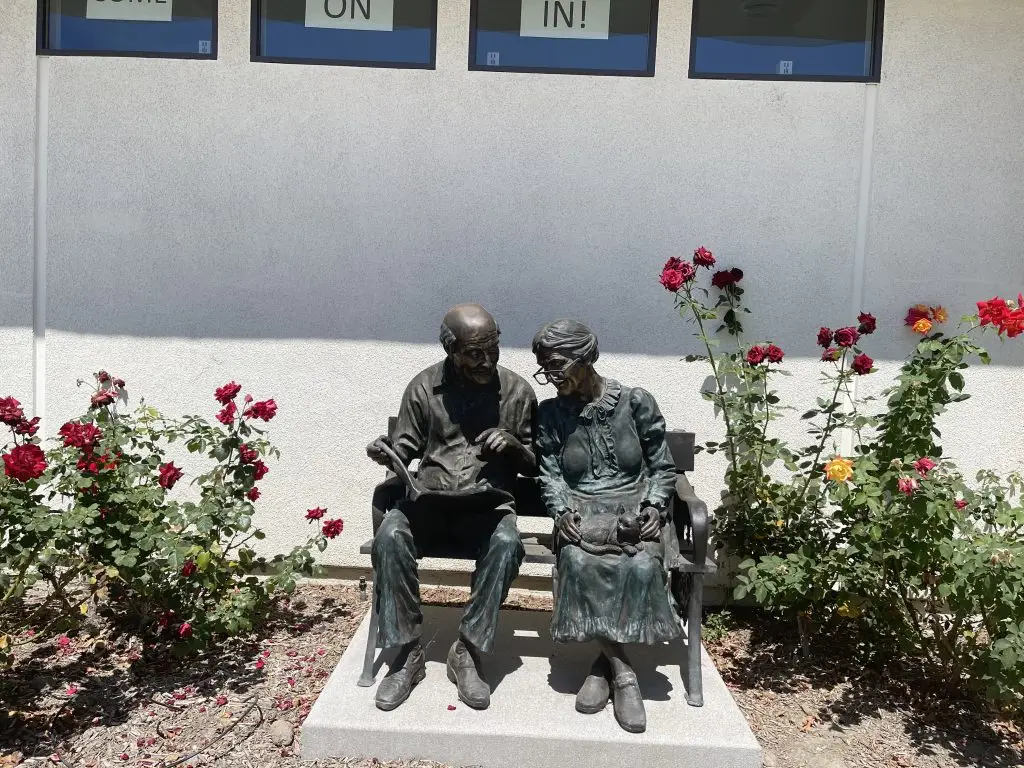 Bronze sculpture of an elderly couple sitting on a bench, surrounded by blooming roses, symbolizing community and companionship in Leisure World retirement living.