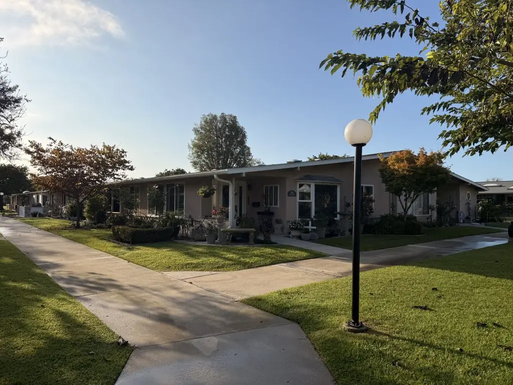 Residential pathway in Leisure World Seal Beach with well-maintained homes, landscaped greenery, and outdoor lighting, illustrating community living for active seniors.