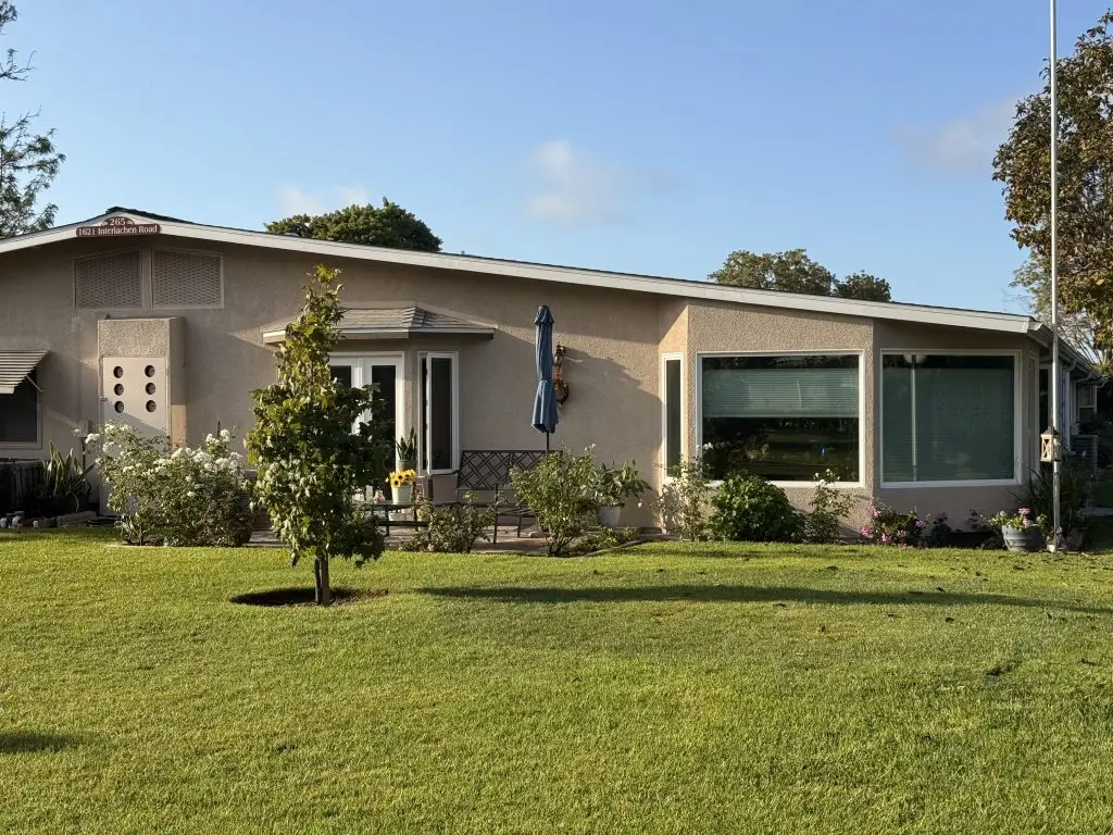Single-story residential home in Leisure World Seal Beach, featuring landscaped yard, patio with umbrella, and large windows, exemplifying maintenance-free living in a coastal retirement community.