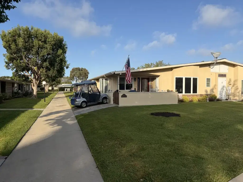 Leisure World Seal Beach community pathway with golf cart, residential units, and American flag, showcasing the inviting coastal lifestyle and recreational amenities.