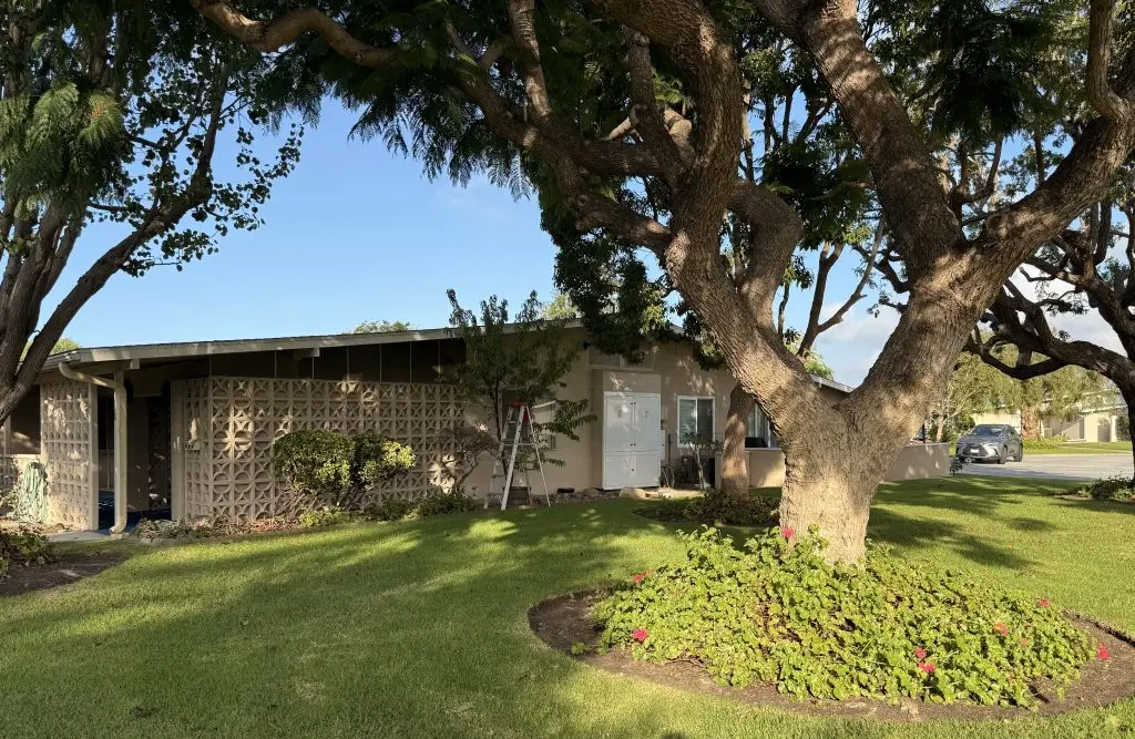 Leisure World home exterior with landscaped yard, mature trees, and a clear blue sky, emphasizing accessibility and low-maintenance living for seniors.