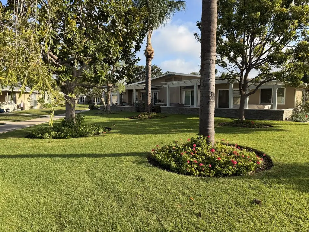 Lush green landscape of Leisure World Seal Beach, featuring well-maintained homes and vibrant flower beds, emphasizing proximity to recreational amenities and community living for active seniors.