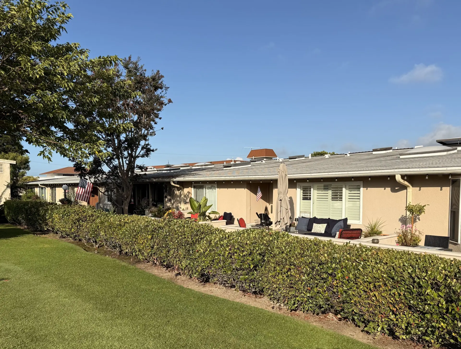 Leisure World Seal Beach residential exterior featuring well-maintained landscaping, patio seating, and an American flag, illustrating the community's inviting atmosphere for 55+ living.