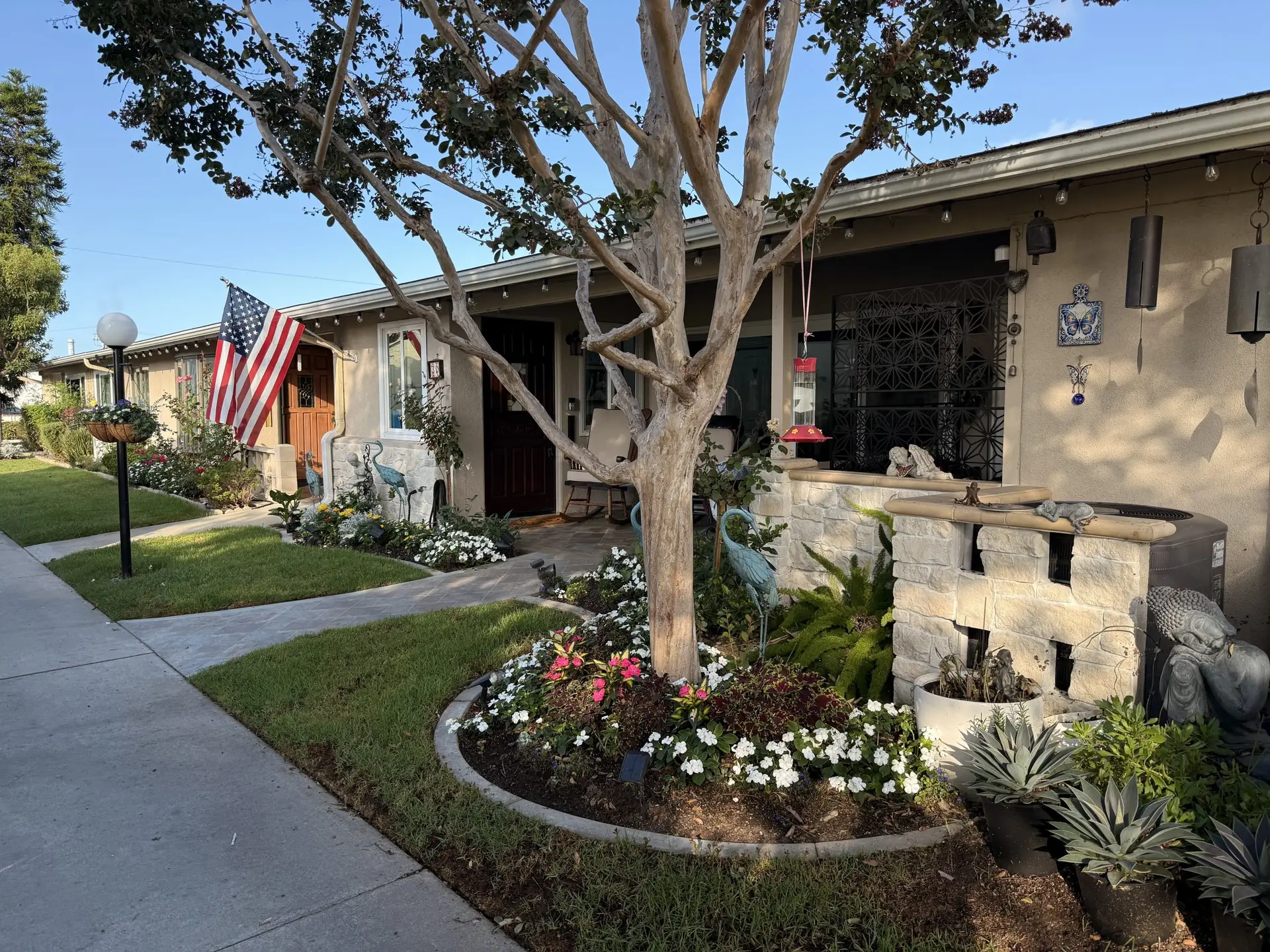 Charming Leisure World Seal Beach home exterior with American flag, vibrant flower beds, decorative garden statues, and a welcoming atmosphere for active 55+ community lifestyle.