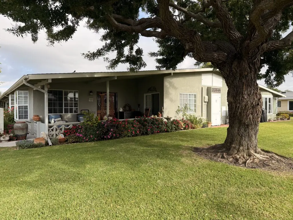 Leisure World Seal Beach home with landscaped front yard, featuring a large tree and colorful flowers, symbolizing the community's appealing real estate options.