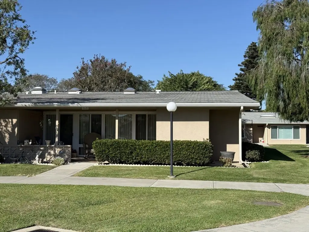 Single-story residential building in Leisure World Seal Beach, featuring manicured hedges, a porch with seating, and nearby landscaped common areas, reflecting community living and maintenance standards.