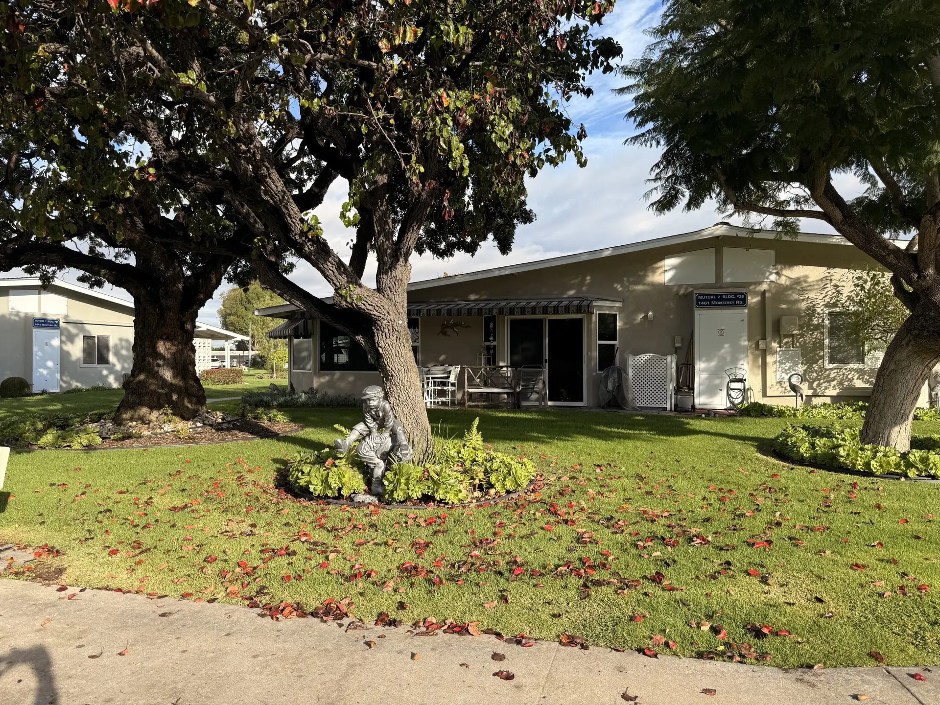 Leisure World Seal Beach community landscape featuring a charming home, mature trees, and a decorative statue amidst colorful fallen leaves, illustrating the vibrant living environment for active retirees.