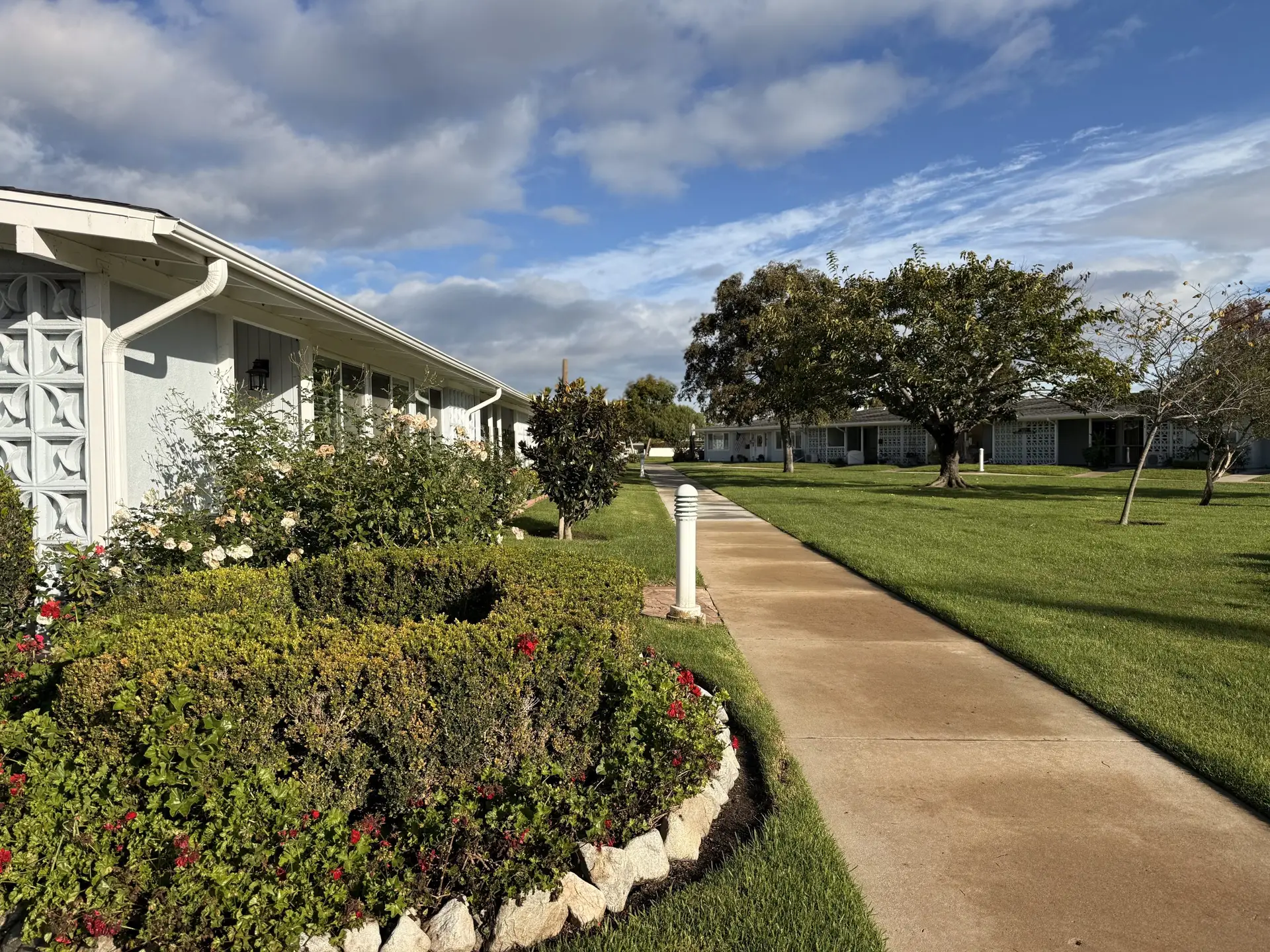 Pathway through landscaped gardens and residential buildings in Leisure World community, Seal Beach, showcasing vibrant greenery and a sunny sky.