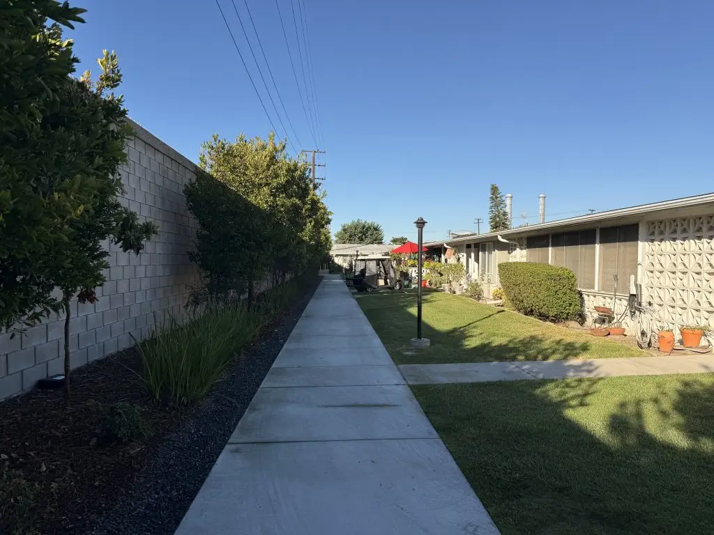 Pathway lined with greenery leading to Leisure World Seal Beach residences, showcasing well-maintained landscaping and community amenities.