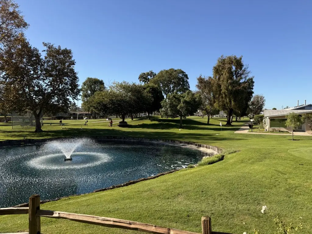 Community pond with fountain, surrounded by lush green lawns and trees, illustrating the tranquil outdoor amenities of Leisure World, a 55+ community in Seal Beach.