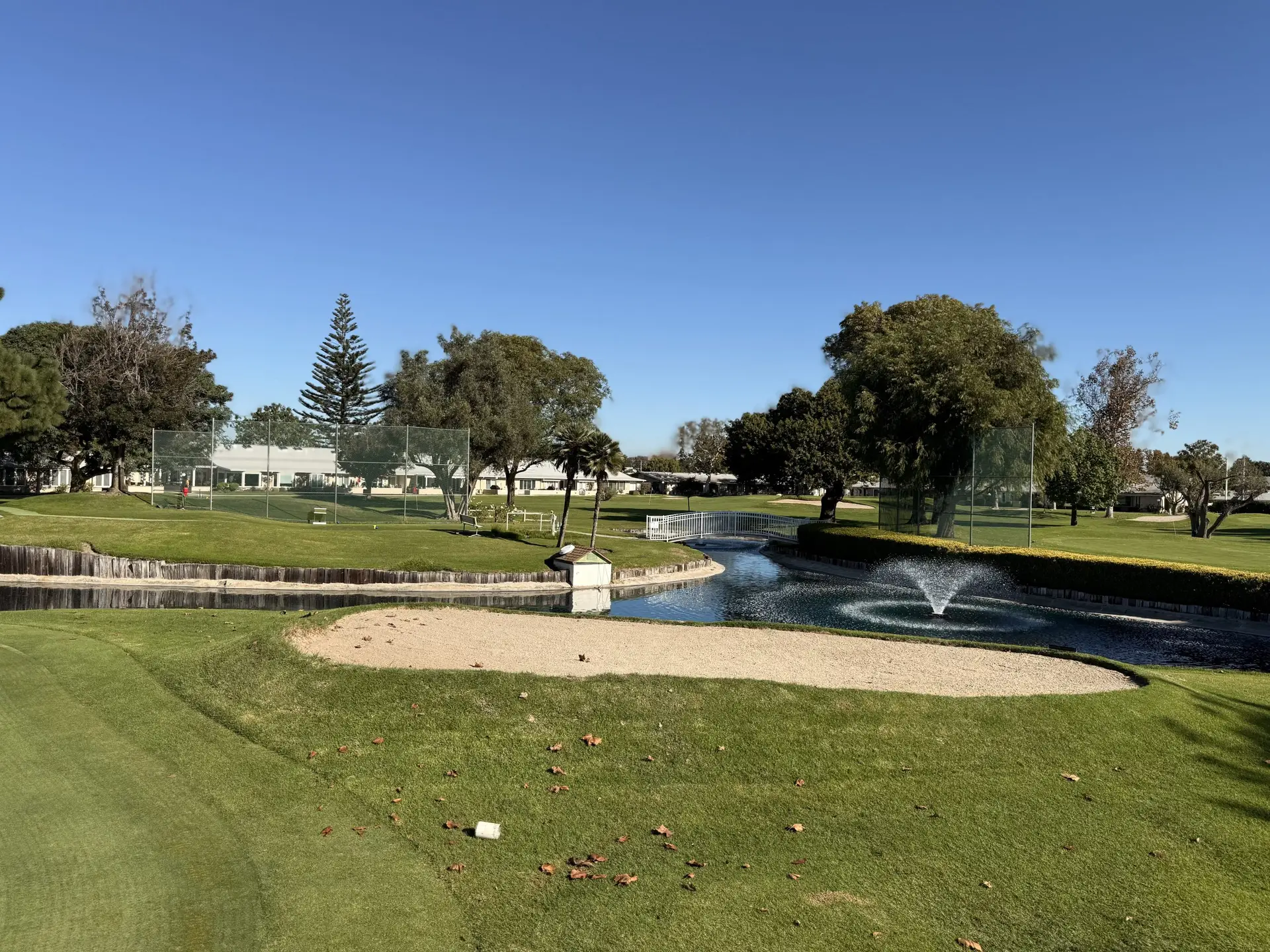 Golf course view in Leisure World Seal Beach featuring a water fountain, manicured lawns, and residential buildings, highlighting the community's amenities for the 55+ lifestyle.