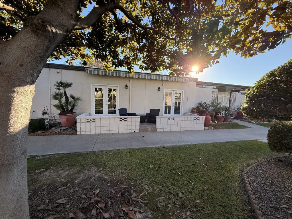 Exterior view of a Leisure World residence with landscaped garden, featuring a pathway, potted plants, and seating area, emphasizing community living for active seniors.