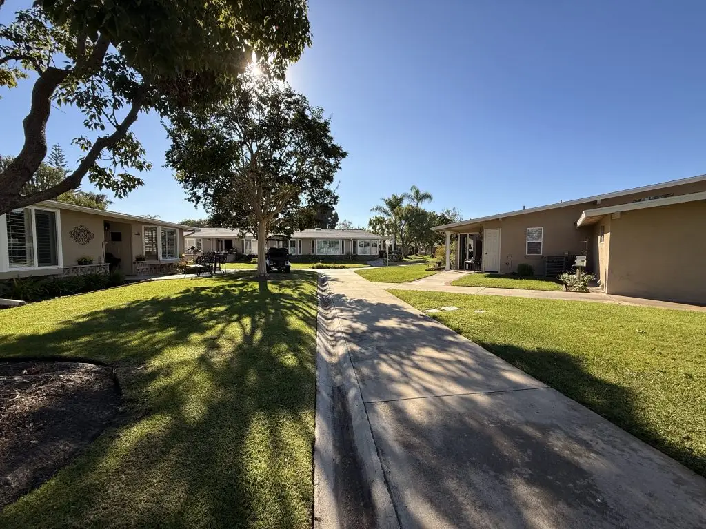 Pathway through a well-maintained community with single-story residences, landscaped lawns, and trees, reflecting the active adult lifestyle in Leisure World Seal Beach.