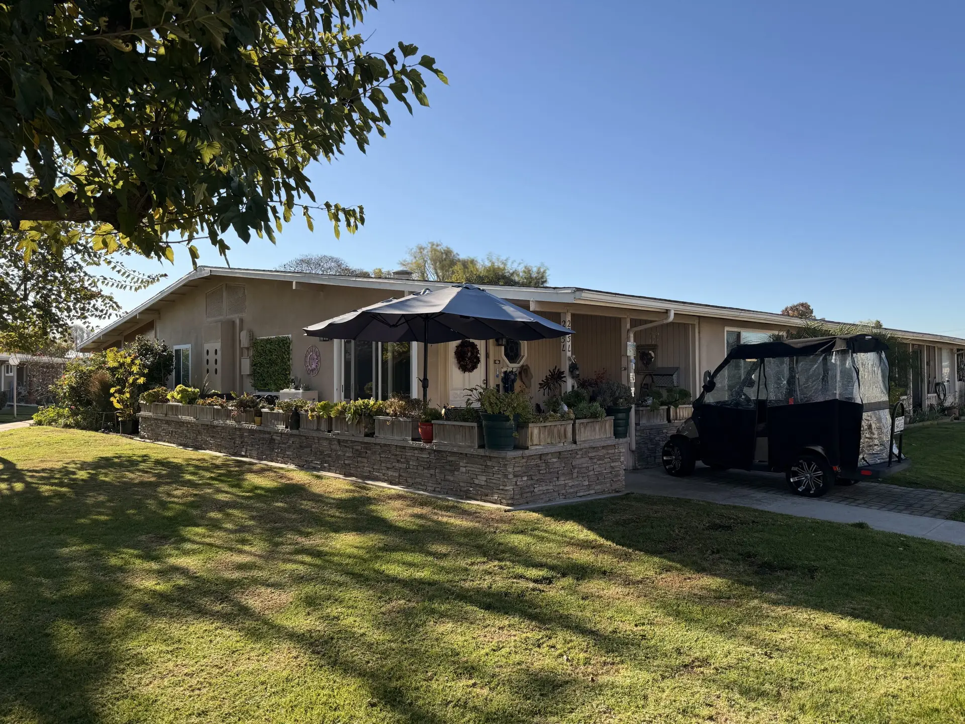 Leisure World residence featuring a well-maintained exterior, lush landscaping, and a black golf cart parked in the driveway, representing affordable living in a 55+ community.