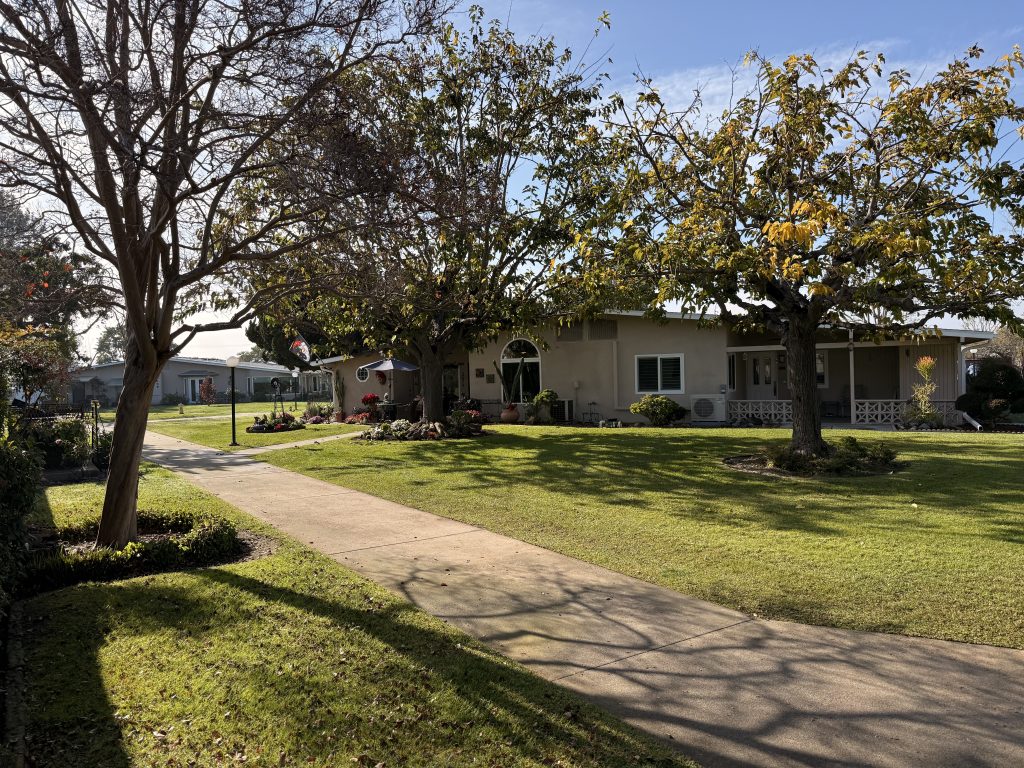 Landscaped pathway leading to a well-maintained home in Leisure World, surrounded by vibrant gardens and trees, illustrating community living and outdoor maintenance.
