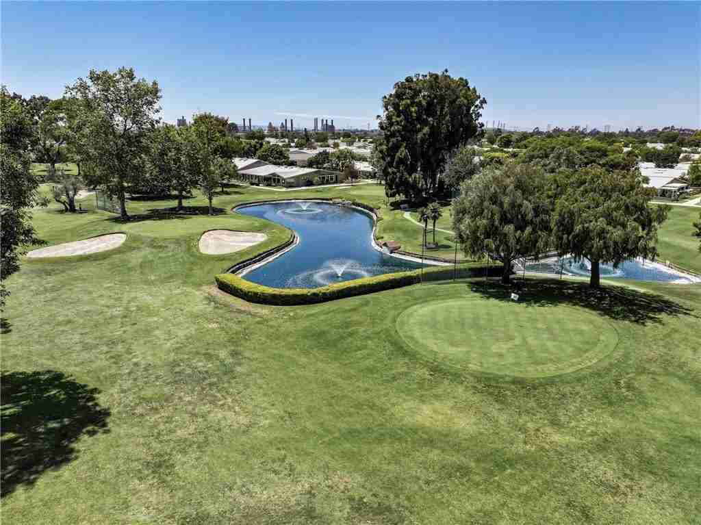 Aerial view of a golf course with a winding pond, lush greenery, and residential properties in Leisure World Seal Beach, highlighting community amenities and outdoor living.