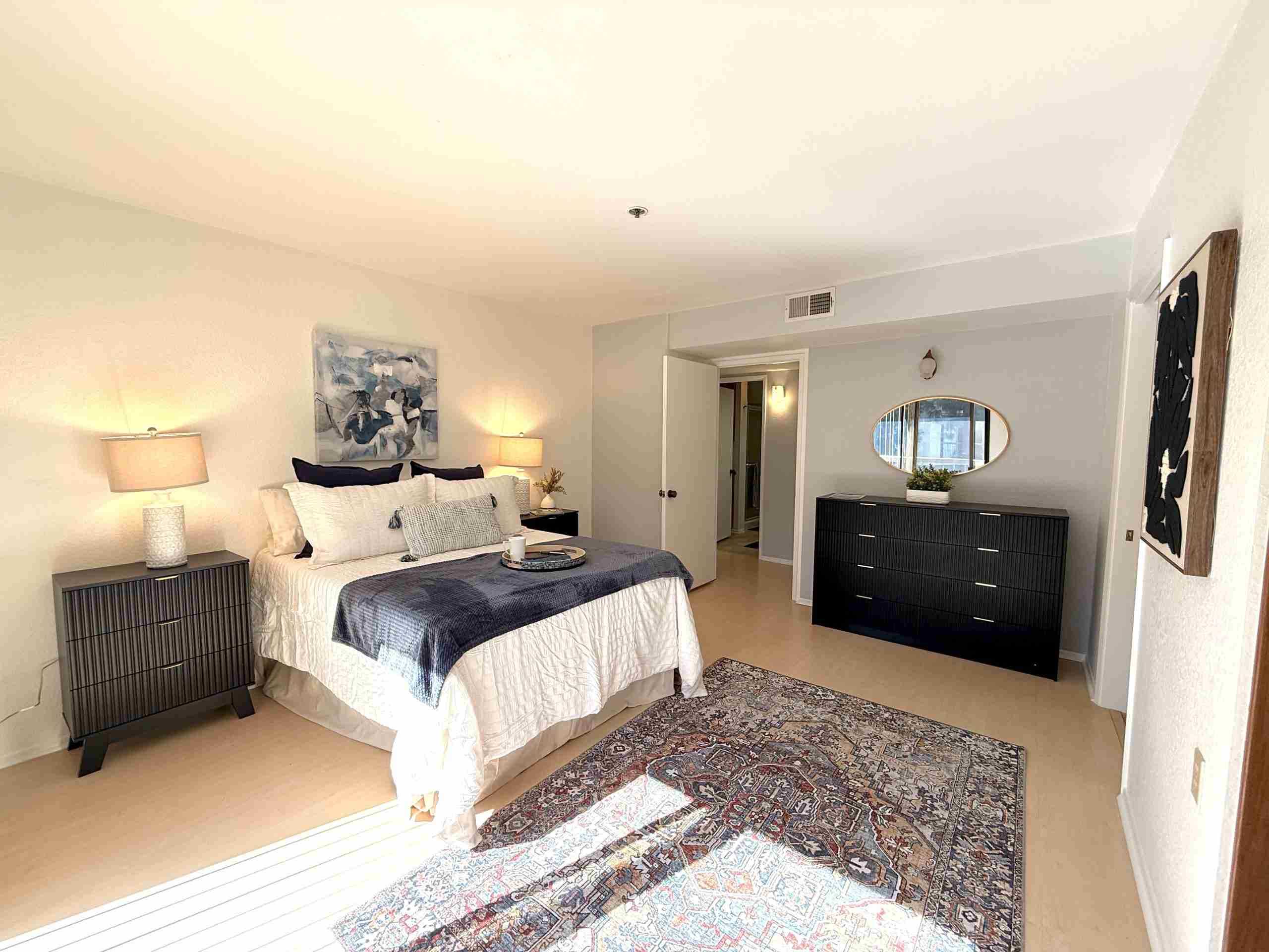 Spacious bedroom in Leisure World Seal Beach featuring a neatly made bed, stylish nightstands with lamps, a decorative area rug, and modern dresser, emphasizing comfort and appeal for potential buyers in a 55+ community.