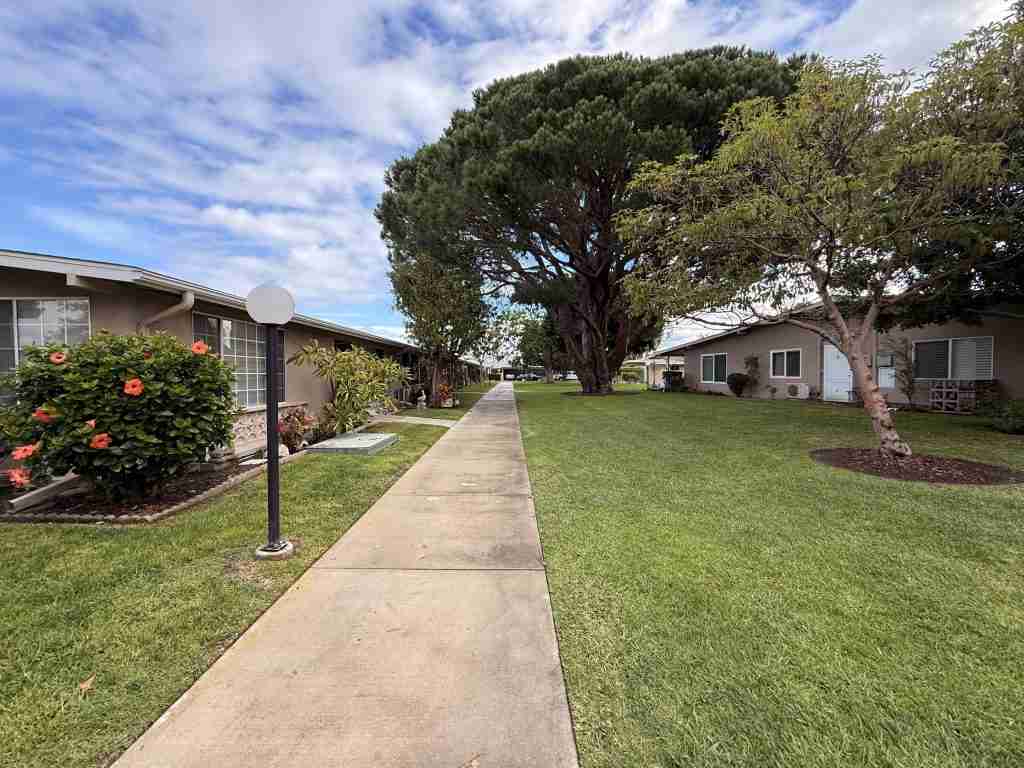Pathway through Leisure World Seal Beach community with landscaped gardens, residential buildings, and large trees.