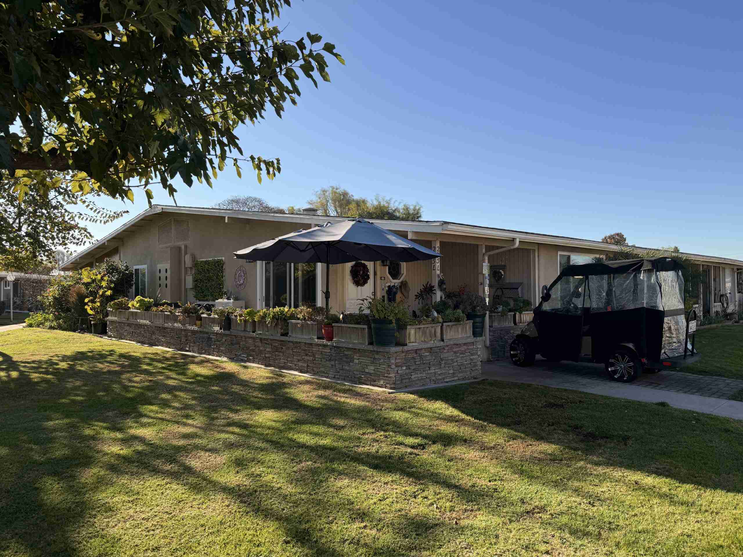 Charming home in Leisure World Seal Beach with lush landscaping, outdoor umbrella, and golf cart, showcasing community's vibrant lifestyle and amenities.